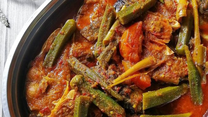 Ikan patin dimasak asam pedas Melaka dengan kuah merah pekat, lengkap dengan bendi, daun kesum dan bunga kantan