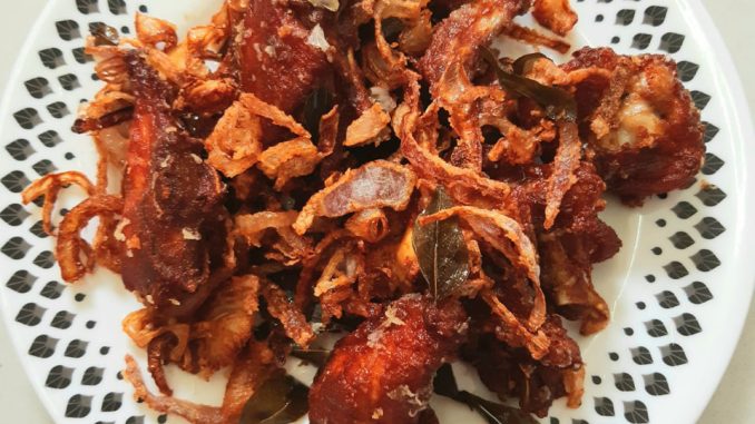 Ayam goreng berempah garing dengan bawang goreng dan daun kari dihidang atas pinggan