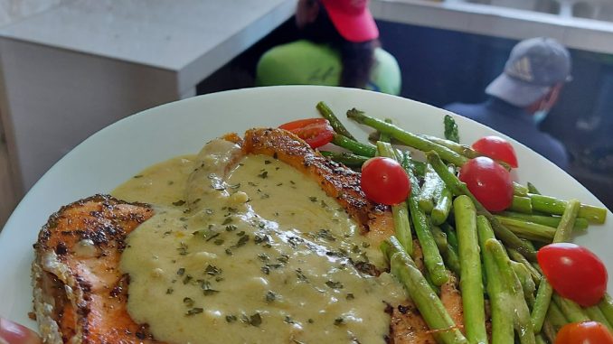 Salmon panggang disiram dengan sos lemon berkrim dan taburan parsley segar, sesuai untuk hidangan istimewa.