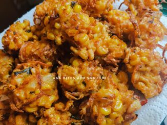 Cucur jagung sedap berwarna keemasan disusun dalam pinggan putih bersama cili merah dan daun kari