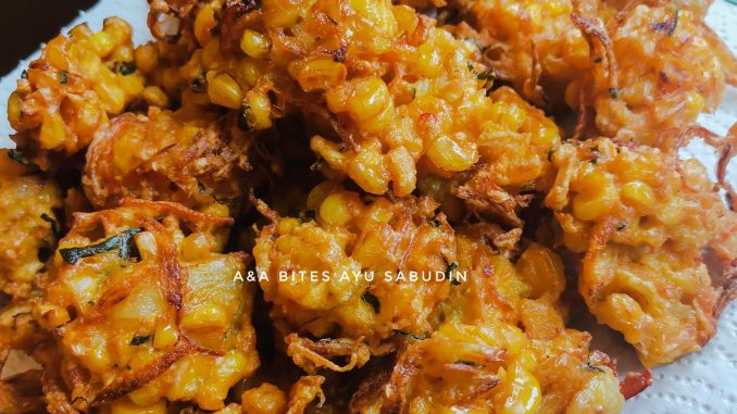 akak pesan Cucur jagung sedap berwarna keemasan disusun dalam pinggan putih bersama cili merah dan daun kari