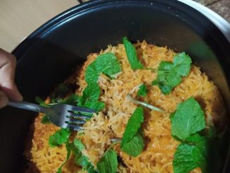 Nasi tomato basmathi yang siap dimasak, berwarna merah keemasan, dihias dengan daun ketumbar dan bawang goreng, dihidang dalam pinggan putih.