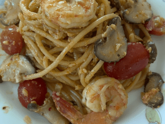 Spaghetti tomyam berkrim bersama udang, tomato ceri dan daun limau purut dalam pinggan putih.