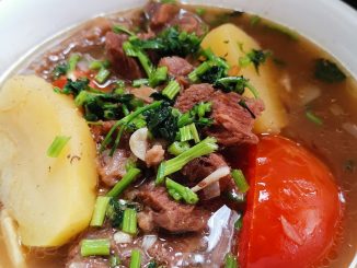 Sup daging Thai ala tomyam berwarna merah dengan kentang, tomato, cili api dan daun sup sebagai hiasan.