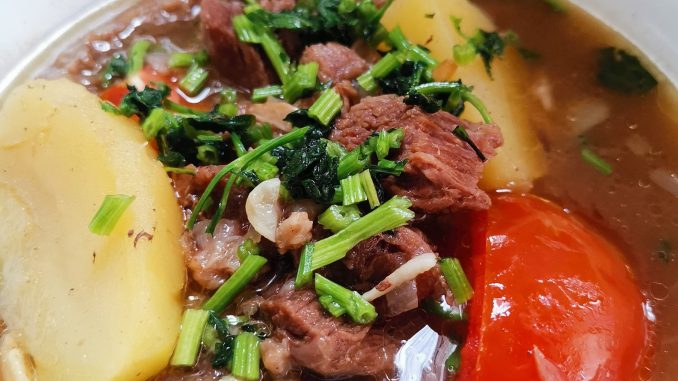 Sup daging Thai ala tomyam berwarna merah dengan kentang, tomato, cili api dan daun sup sebagai hiasan.