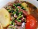 Sup daging Thai ala tomyam berwarna merah dengan kentang, tomato, cili api dan daun sup sebagai hiasan.
