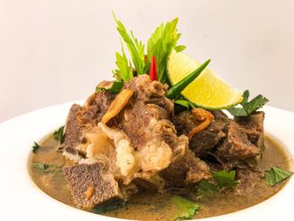 Semangkuk sup tulang lembu panas berasap dengan tulang gearbox, ditabur daun bawang dan bawang goreng, dihidang bersama sambal kicap.