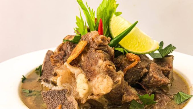Semangkuk sup tulang lembu panas berasap dengan tulang gearbox, ditabur daun bawang dan bawang goreng, dihidang bersama sambal kicap.