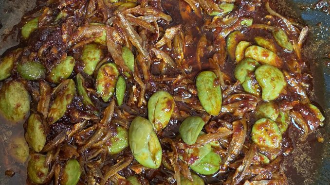 Sambal ikan bilis petai siap dimasak, berwarna merah pekat dengan petai dan ikan bilis goreng, dihidang dalam pinggan putih.