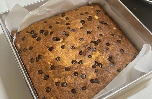 Kek pisang bakar yang gebu dan keemasan dalam loyang, ditabur cip coklat di atas.