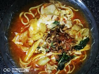 Mee Bandung dengan kuah pekat berwarna kemerahan, dihidangkan bersama ayam, udang, tomato dan sayur-sayuran segar, siap untuk dimakan.