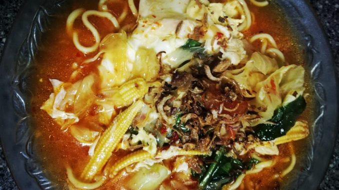 Mee Bandung dengan kuah pekat berwarna kemerahan, dihidangkan bersama ayam, udang, tomato dan sayur-sayuran segar, siap untuk dimakan.