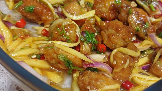 Hidangan Ayam Mangga rangup dengan sos mangga pedas manis, dihias dengan hirisan cili padi dan daun ketumbar dalam pinggan putih.