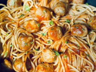 Spaghetti meatballs dengan sos tomato pekat, taburan daun parsli dan keju parmesan parut di atasnya.