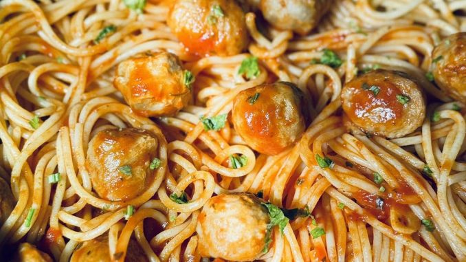 Spaghetti meatballs dengan sos tomato pekat, taburan daun parsli dan keju parmesan parut di atasnya.