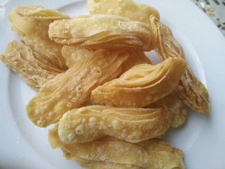 Kuih Tiram rangup, keemasan, dihias gula kastor, tersusun kemas dalam pinggan putih.