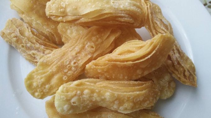 Kuih Tiram rangup, keemasan, dihias gula kastor, tersusun kemas dalam pinggan putih.