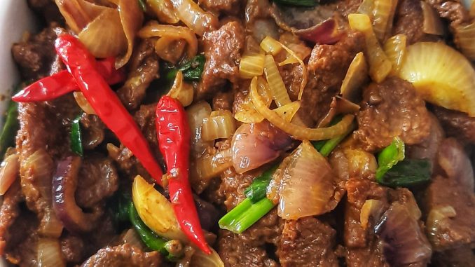 Daging goreng kunyit basah berwarna keemasan dengan hirisan bawang dan cili