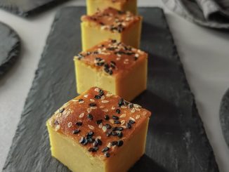 Bingka durian kuning lemak manis, dihias dengan bijan putih dan hitam, dipotong segi empat di atas pinggan, sedia untuk dihidangkan.