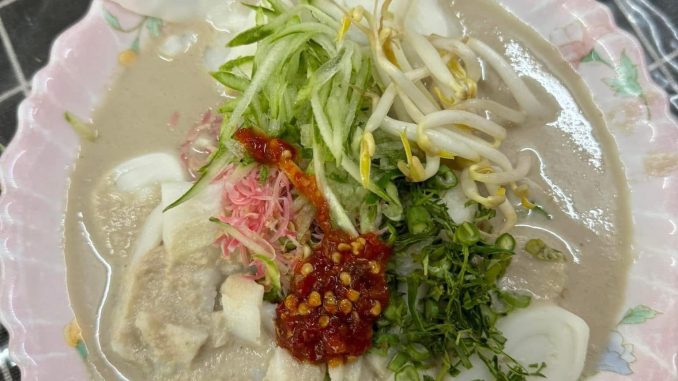 Kuah laksam berlemak, pekat dan beraroma dengan ikan segar, santan kaya, dan ulam meriah seperti timun dan bunga kantan.