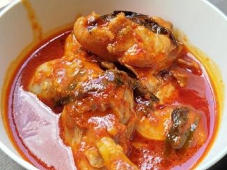 Asam pedas ayam Johor berkuah pekat berwarna merah, dihidangkan panas dengan daun kesum dan bendi