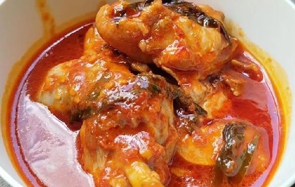 Asam pedas ayam Johor berkuah pekat berwarna merah, dihidangkan panas dengan daun kesum dan bendi