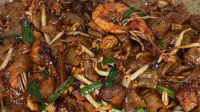Kuetiau goreng seafood dengan udang, sotong dan sayur segar di dalam kuali.